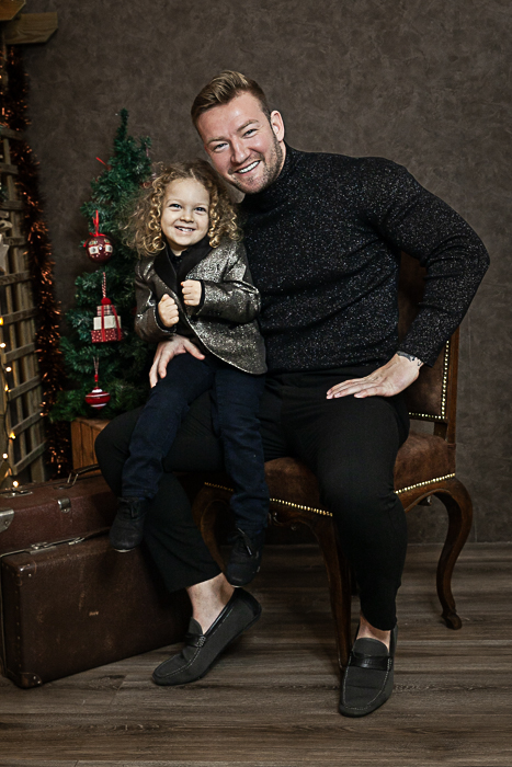 a fiú öleli a lányt a fehér kanapén ülve, háttérben karácsonyi fények - karácsonyi páros fotózás debrecen