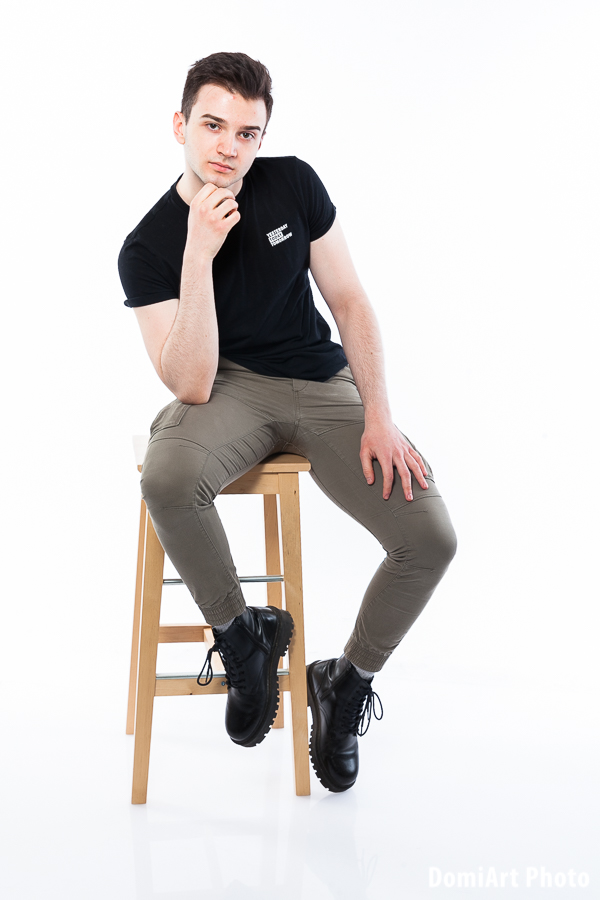 Fiú ül a fa mintájú bárszéken, egyik lába a lábtartón, a másik a földön. Férfi portré fotózás debrecen
