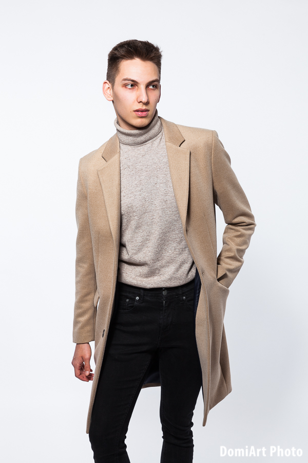 elegáns fiatalember ül egy fa bárszéken, egyik lábát a szék lábtámaszán tartva, zakót fog a vállán - férfi fotózás Debrecen