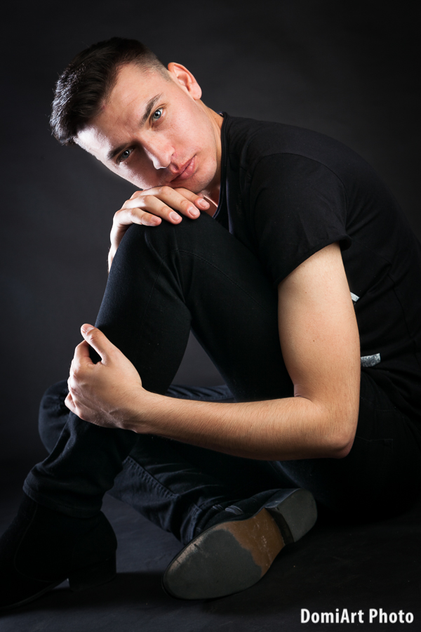 férfi ül a földön, a térde fel van emelve, rákönyököl és ránk néz, komoly tekintettel. Férfi portré fotózás