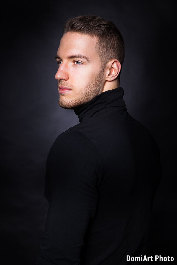 klasszikus közeli férfi portréfotózás, félig visszanéző arc, feketre háttérrel