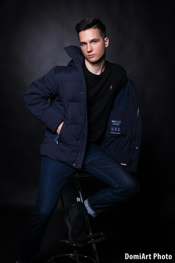 férfi veszi le a kabátját egy fekete háttér előtt, egy bárszéken ülve, a kamerába nézve - portré fotózás debrecen