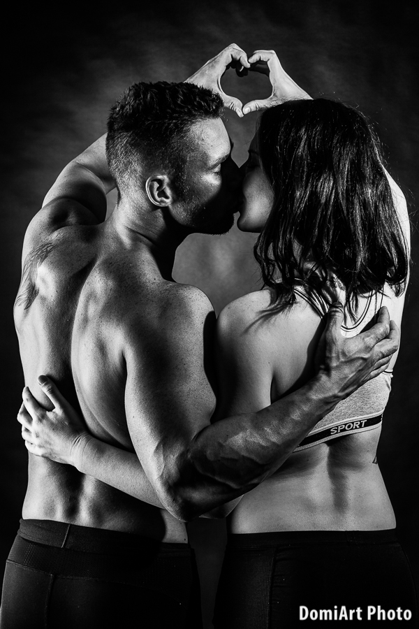 A férfi és a női fitness modell oldalt állnak egymás mellett és a kezükkel szivecskét formáznak - fitness fotózás debrecen