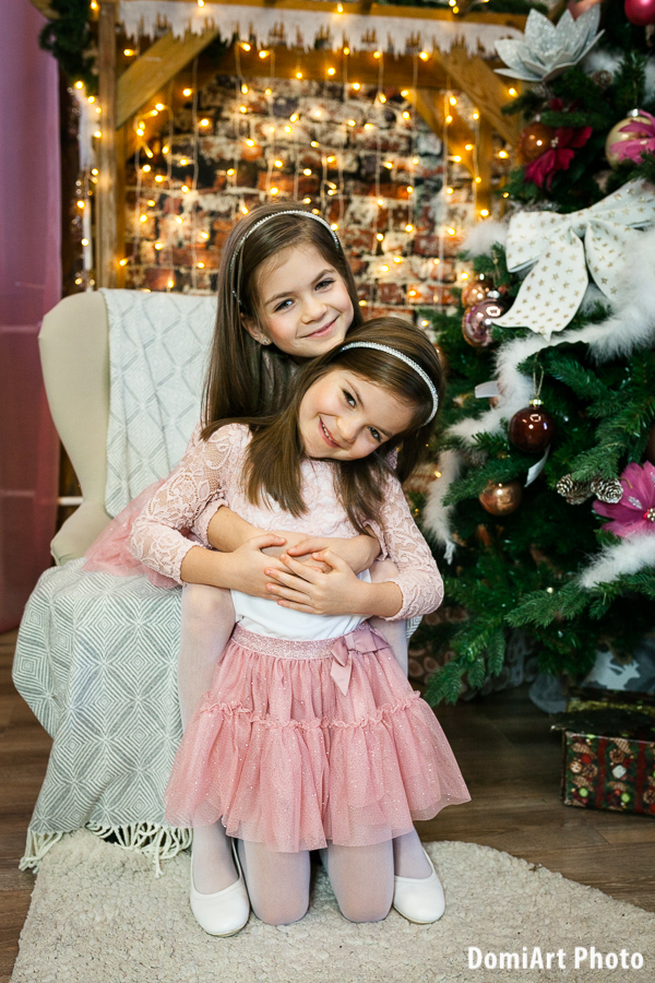 két lánytestvér a karácsonyi ledes háttér előtt, téglafalas épített háttér