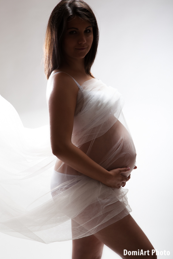 felülről világított kép, amikor az álló kismama be van takarva egy fügönnyel, mögötte persze fehérneműben áll.