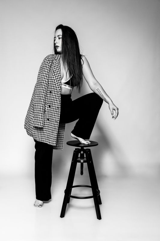 fashion glamour fekete-fehér kidolgozásban sejtelmes fényben ülő félakt nő, aki hajával és karjával takarja a melleit