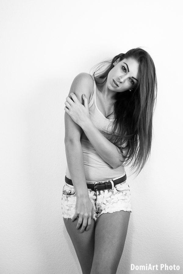 fejét balra döntő modell a fal mellett erős modell pózban áll fehér atlétában és farmer nadrágban - modell portfólió fotózás debrecen