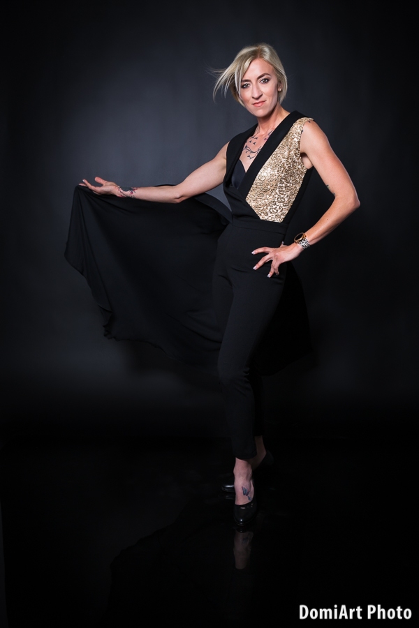 fekete hátteres fotózáson a modell a fekete szoknyáját fogja a jobb kezében, miközben a kamerába figyel. Műtermi fotózás Debrecen.